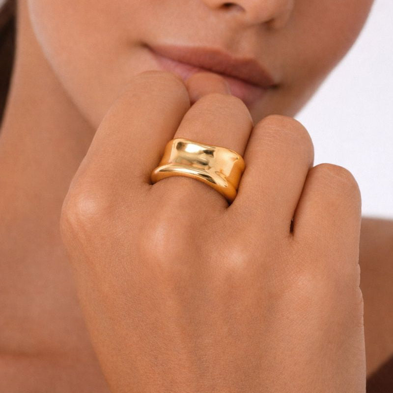 Close-up of a hand wearing a gold ring with a blurred background