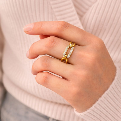 Close-up of a hand wearing a gold ring with a light pink sweater and denim jeans.