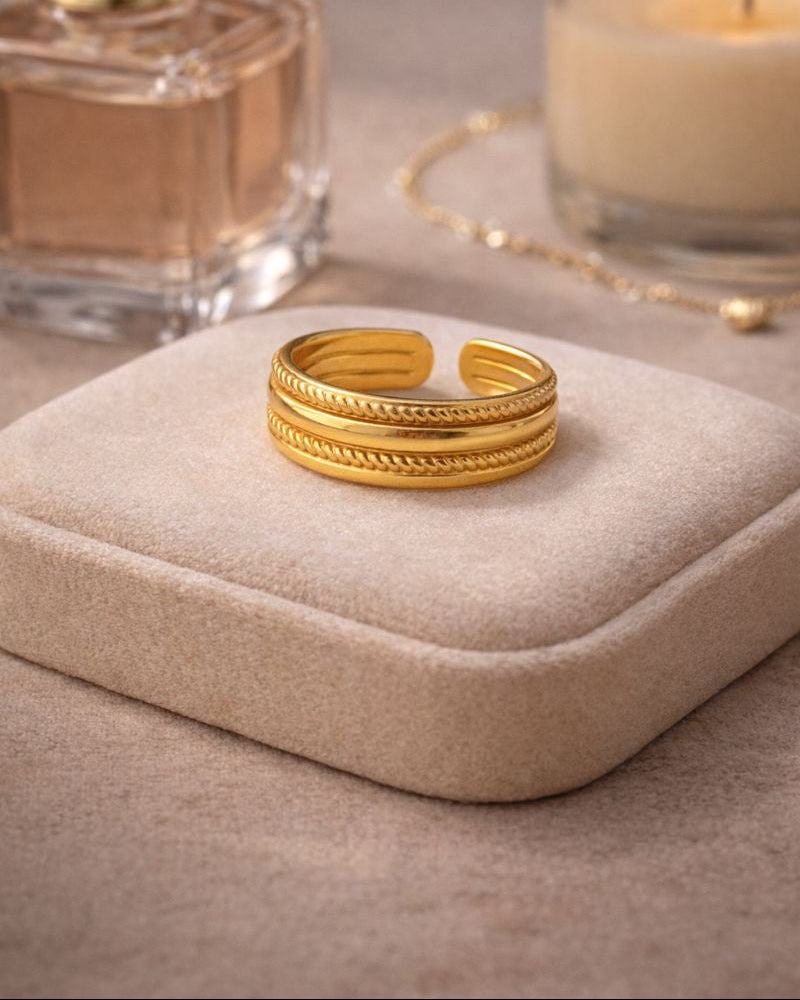 Gold ring on a jewelry box with a candle and perfume bottle in the background