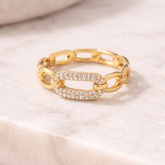 Gold chain-link ring with embedded stones on a soft beige background