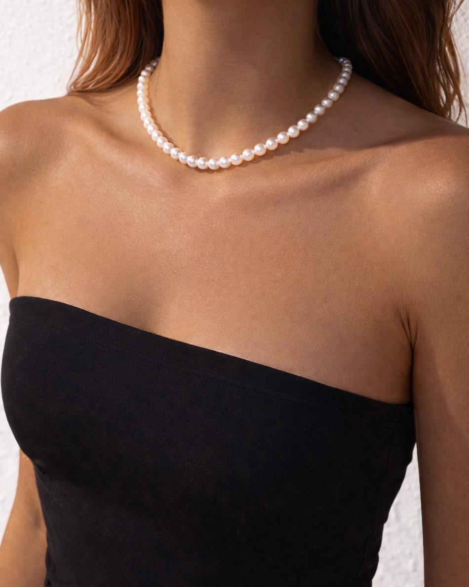 Pearl necklace worn by a person in a black strapless top against a neutral background